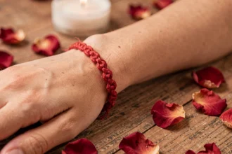 Bracelet fil rouge à 7 nœuds porté au poignet d'une femme sur fond de bois naturel avec pétales de roses séchées